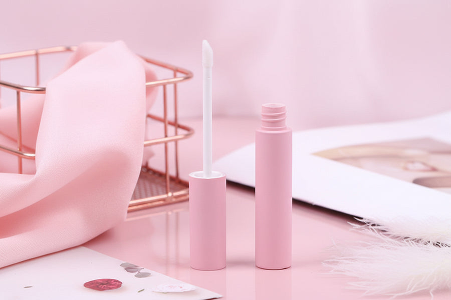 Pink lip gloss tube with applicator on a light surface